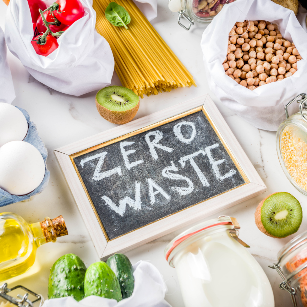 Na środku zdjęcia znajduje się tabliczka z napisem "Zero Waste", a wokół niej różne artykuły spożywcze.