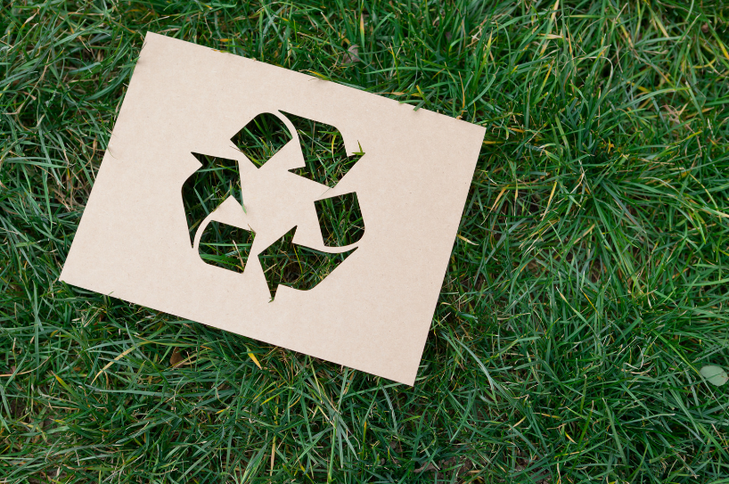 zdjęcie przedstawia wycięty w papierze symbol recyklingu położony na trawie